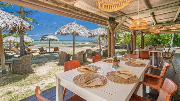 An outdoor dining area with wicker furniture, thatched umbrellas, and a view of the beach. - Villa Tropic Lagoon,  by the lagoon! (Le François)