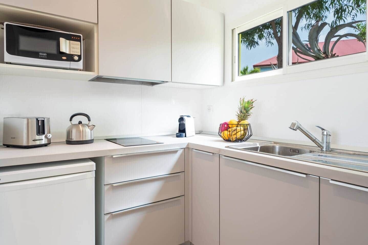A modern kitchen with a microwave, toaster, kettle, and a fruit bowl on the counter.