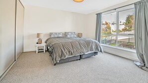 Ein Schlafzimmer mit einem großen Bett, zwei Nachttischen mit Lampen, einem Fenster mit Vorhängen und Blick nach draußen.