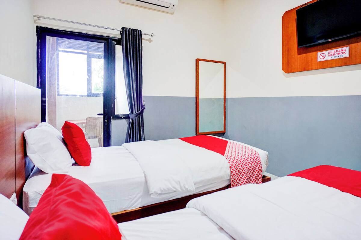A hotel room with two beds, a TV, a mirror, and a window with curtains.