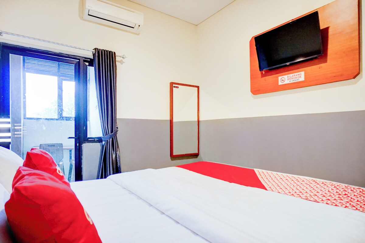 A hotel room with a bed, a television mounted on the wall, a window with curtains, and a door.