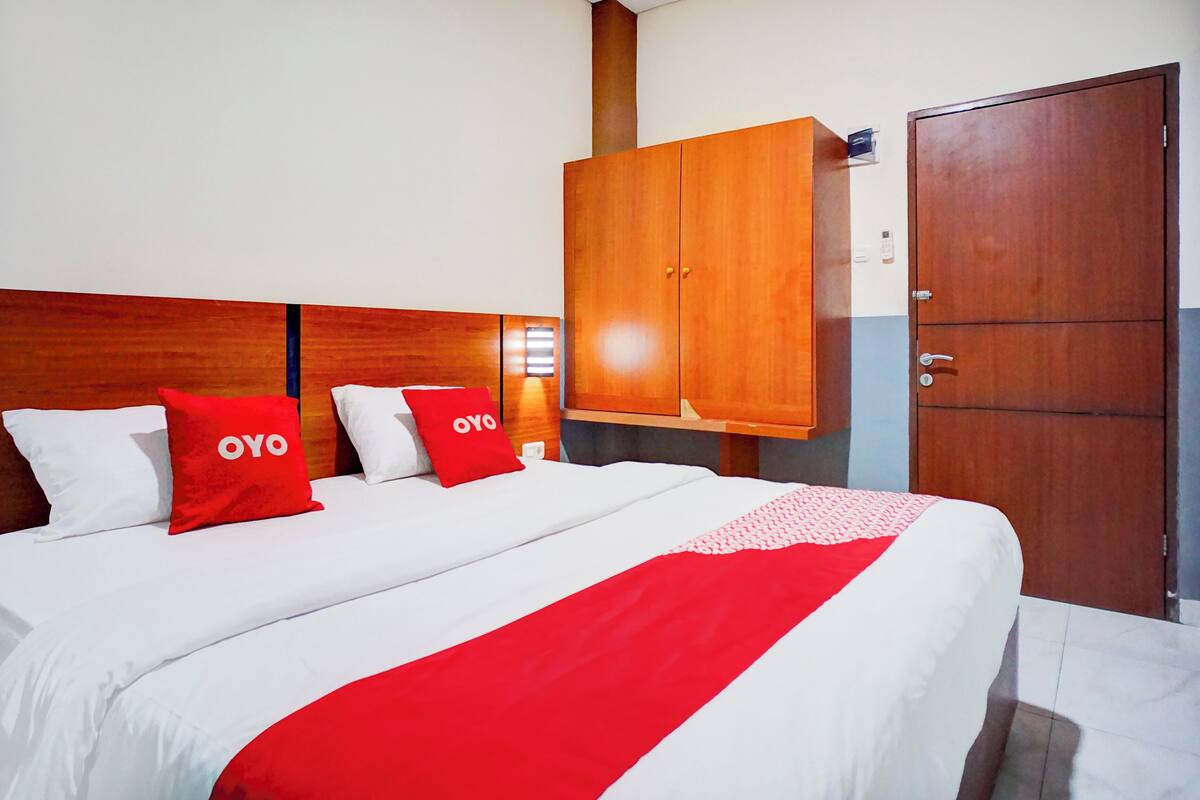 A hotel room with a large bed, two red pillows, a wooden wardrobe, and a door.