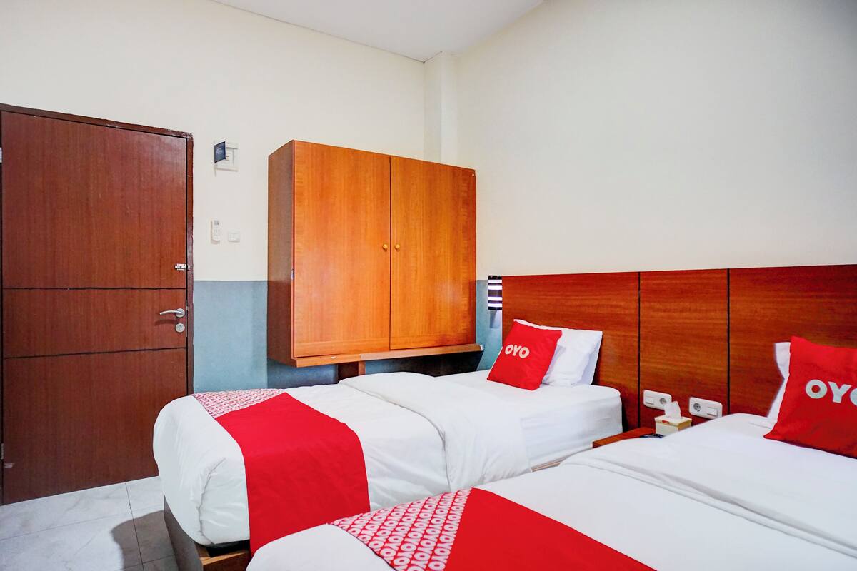 A hotel room with two beds, a wardrobe, and a wooden headboard.