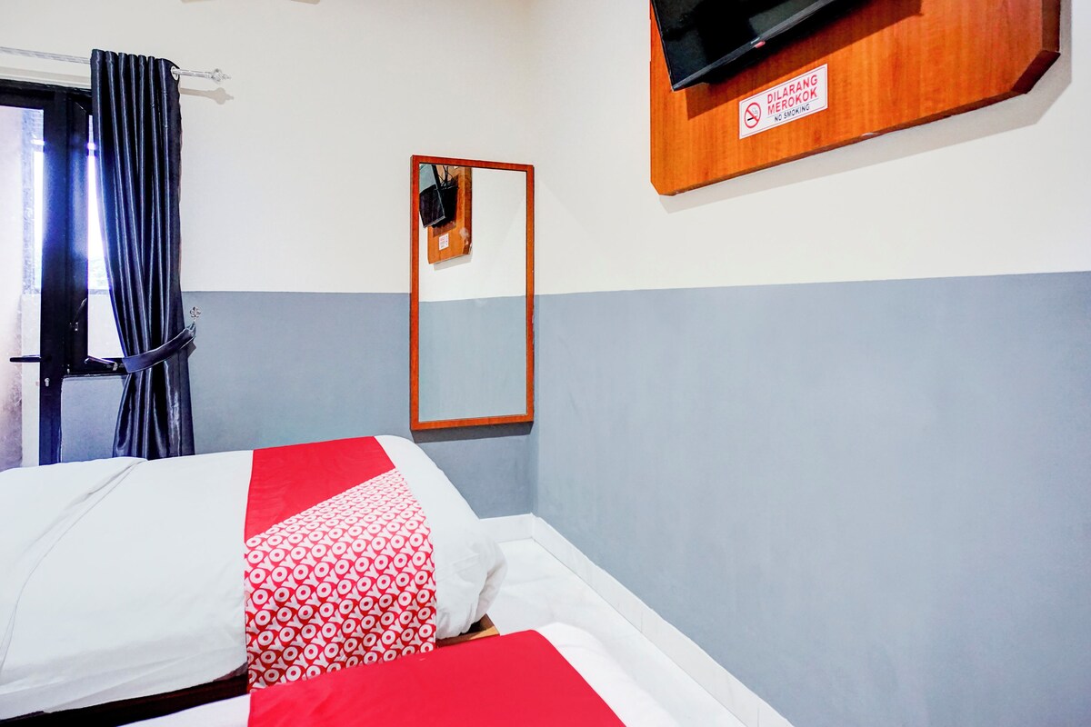 A hotel room with a bed, a TV mounted on the wall, a mirror, and a no-smoking sign.