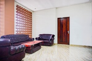 A room with a dark-colored sofa, a smaller armchair, a coffee table, and a wooden door. - Hotel O Sean's Residence Mansyur Near USU (Medan)