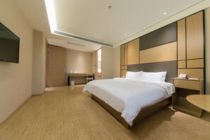 Une chambre d’hôtel avec un grand lit, un bureau, une chaise, une table de chevet et un téléviseur fixé au mur.