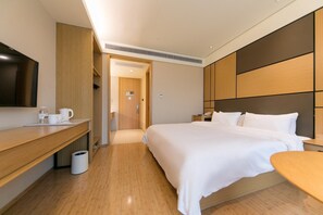 Una habitación de hotel con cama, mesita de noche, televisión y un pequeño escritorio con silla.