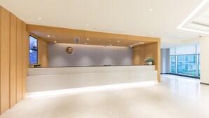 Eine Hotelrezeption mit modernem Design, inklusive einer Rezeption, einem digitalen Bildschirm und einem großen Fenster mit Blick nach außen.