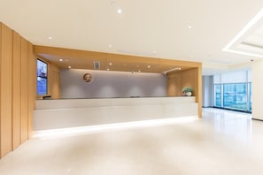 A hotel reception area with a modern design, featuring a reception desk, a digital display, and a large window offering a view of the outside. - Ji Hotel Shanghai Zhangjiang Branch (Shanghai)