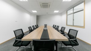 Ein Konferenzraum mit einem langen Tisch, schwarzen Stühlen, weißen Wänden und einem großen Fenster.