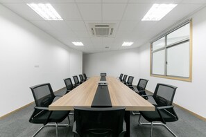 Un salón de conferencias con una mesa larga, sillas negras, paredes blancas y un ventanal grande.