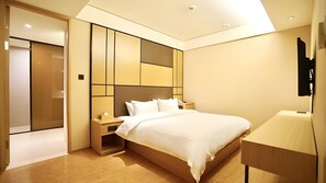 Une chambre d’hôtel moderne dotée d’un grand lit, d’une table de chevet, d’une armoire intégrée et d’un téléviseur à écran plat fixé au mur.