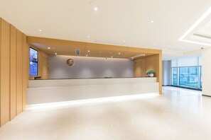 Un espace d’accueil d’hôtel au design moderne, comprenant un comptoir d’accueil, un écran numérique et une grande fenêtre offrant une vue panoramique.
