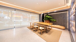 A modern conference room with a wooden table and chairs, a large potted plant, and a view through large windows. - Ji Hotel (Xi'an)