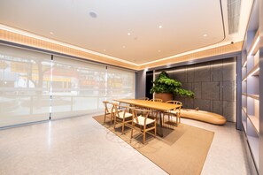 A modern conference room with a wooden table and chairs, a large potted plant, and a view through large windows. - Ji Hotel (Xi'an)