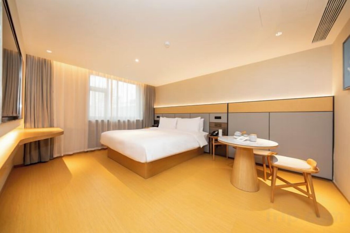 A modern hotel room with a large bed, bedside table, and a small round table with chairs.
