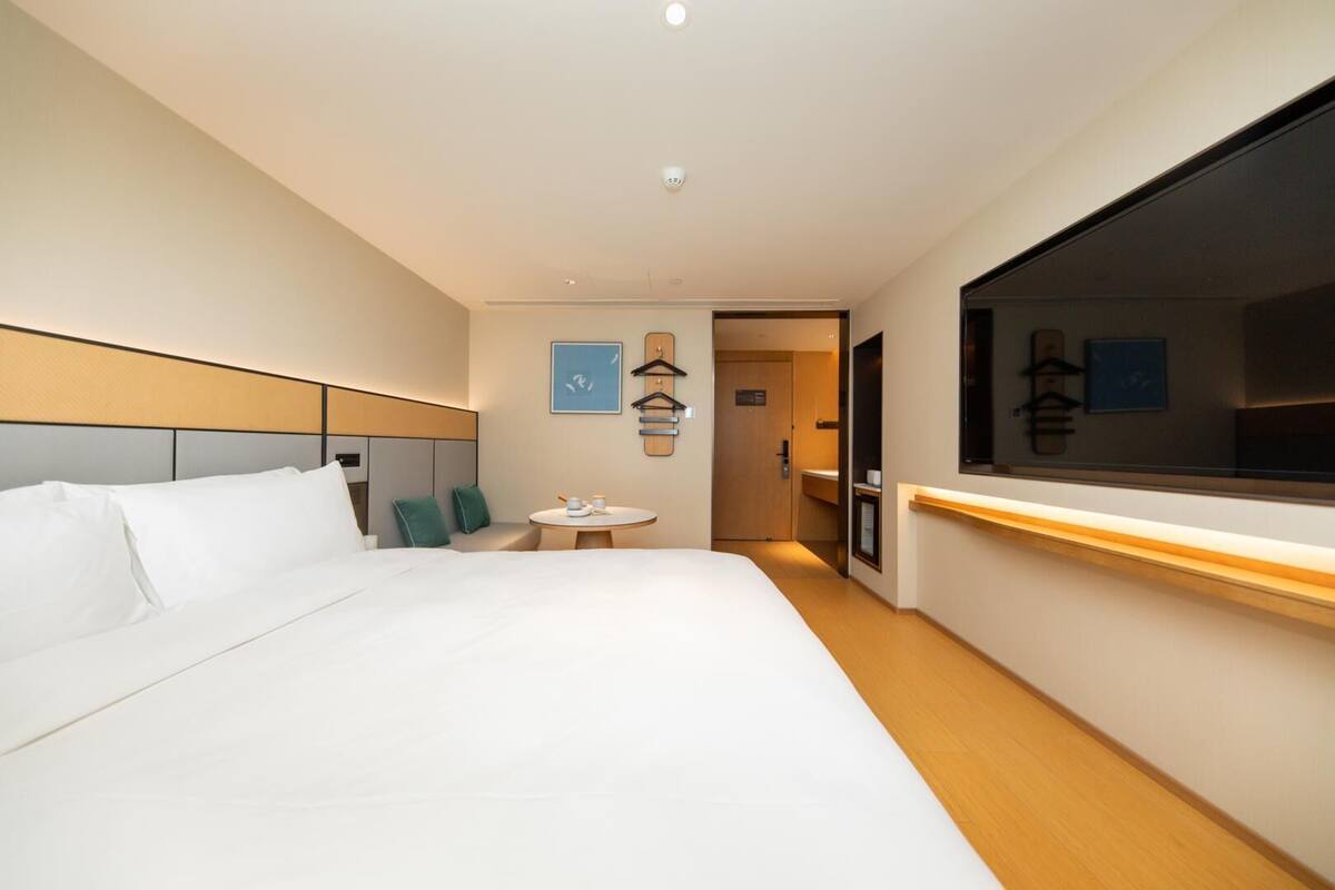 A modern hotel room with a large bed, a bedside table, a small round table, and a large window.