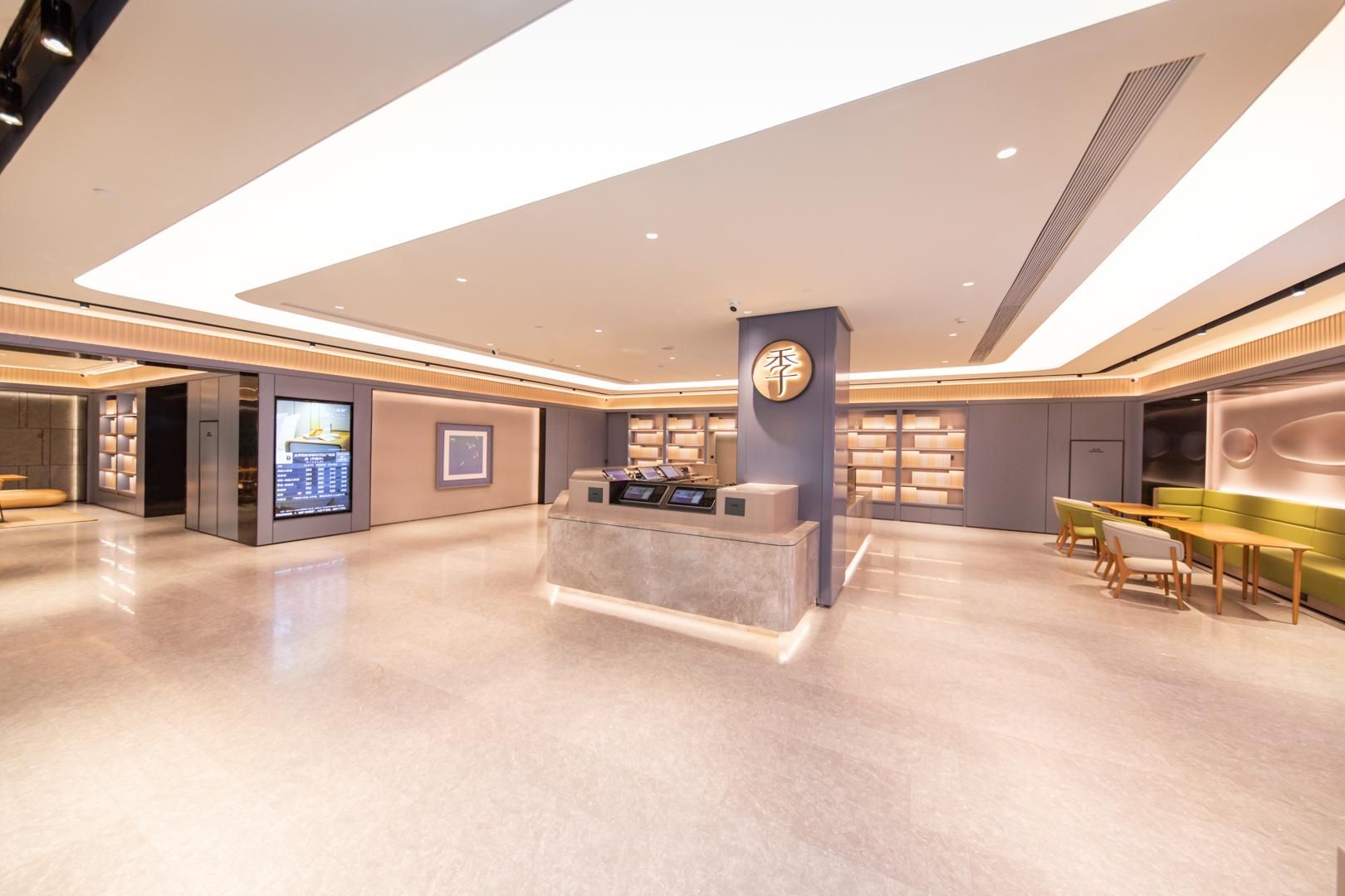 A modern hotel lobby with a reception desk, digital information kiosk, seating area, and a large digital display.