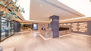 A modern hotel lobby with a reception desk, a digital information kiosk, and a bookshelf.