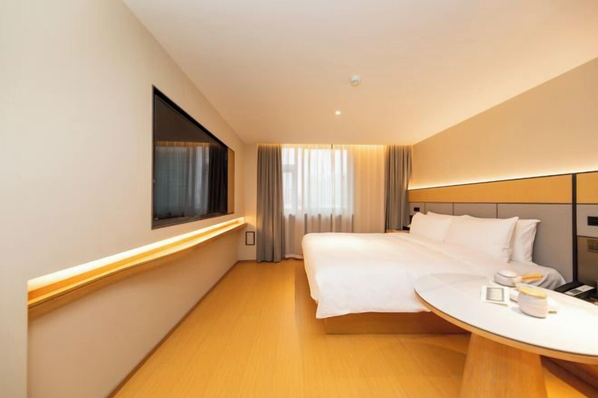 A hotel room with a large bed, bedside table, and a window with curtains.