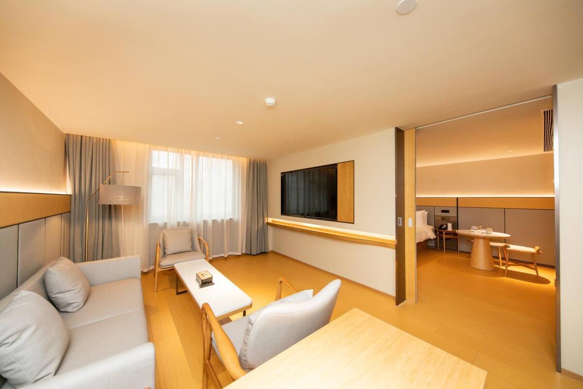 A modern hotel room with a sofa, a dining table, a TV, and a separate dining area.