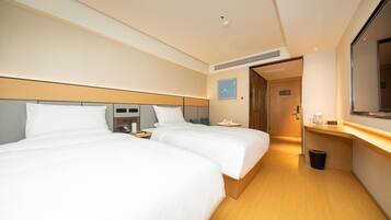 A hotel room with two beds, a desk, a TV, and a bathroom door.