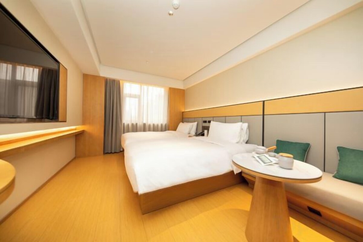 A hotel room with a bed, bedside table, and a seating area with a table and cushions.