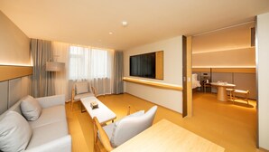 A modern hotel room with a sofa, a dining table, a TV, and a separate dining area. - Ji Hotel (Xi'an)