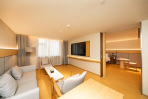 A modern hotel room with a sofa, a dining table, a TV, and a separate dining area. - Ji Hotel (Xi'an)