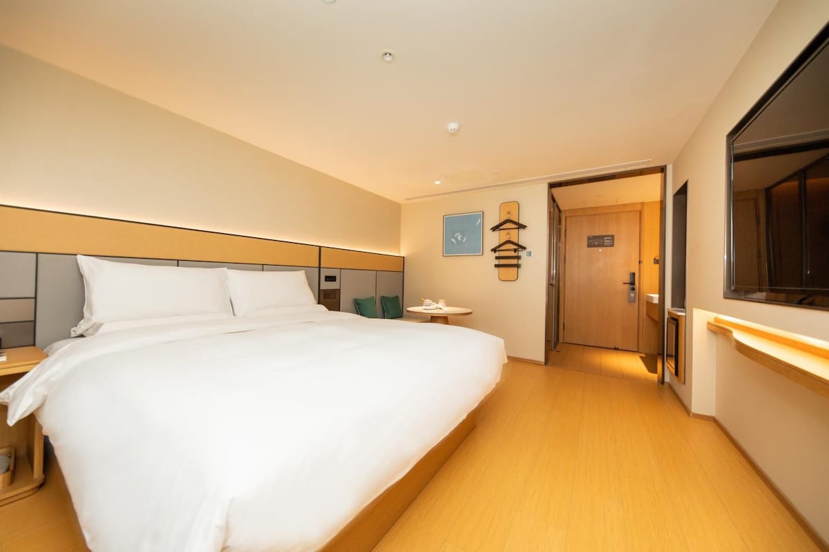 A hotel room with a large bed, a bedside table, a small round table, a wardrobe, and a mirror.