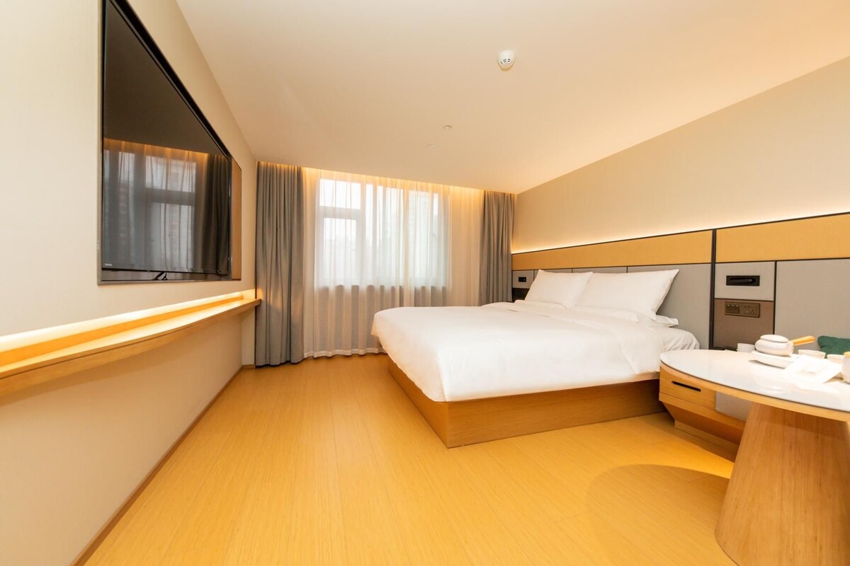 A hotel room with a bed, bedside table, and a window with curtains.