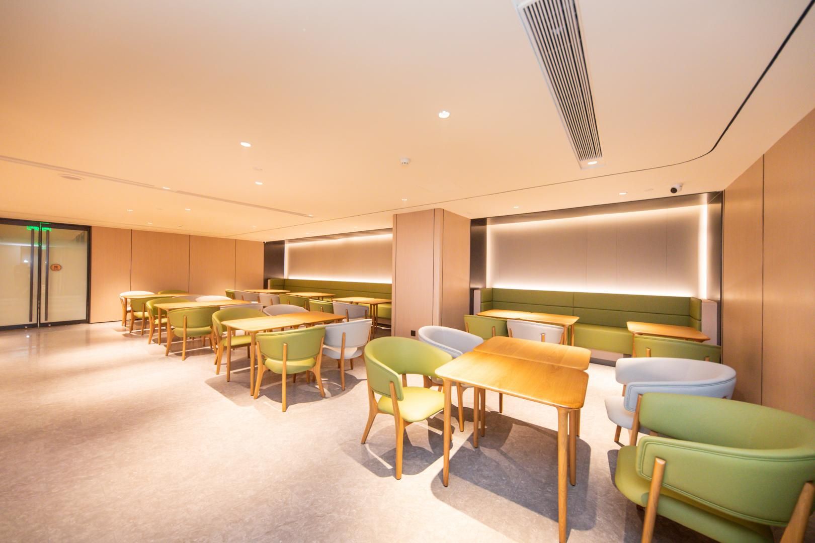 A modern interior with multiple tables and chairs, a large illuminated wall, and a glass door entrance.