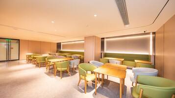 A modern interior with multiple tables and chairs, a large illuminated wall, and a glass door entrance.