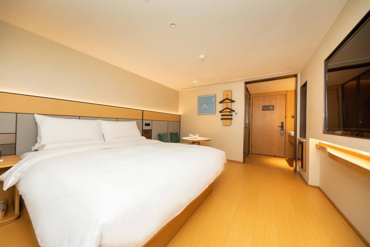 A hotel room with a large bed, a bedside table, a small round table, a wardrobe, and a mirror.