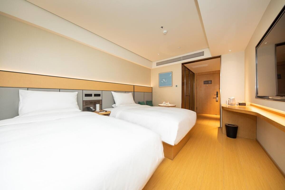 A hotel room with two beds, a desk, a TV, and a bathroom door.