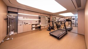 A modern hotel room with a large mirror, a treadmill, a stationary bike, and a compact kitchenette.