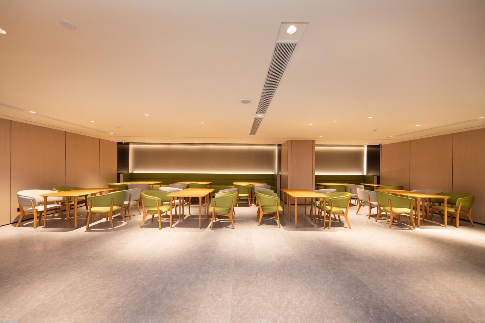 A modern dining area with wooden tables and green chairs, recessed lighting, and a central light fixture.