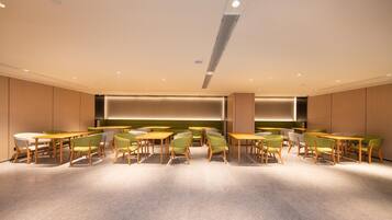 A modern dining area with wooden tables and green chairs, recessed lighting, and a central light fixture.