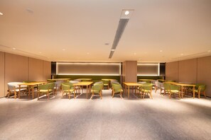 A modern dining area with wooden tables and green chairs, recessed lighting, and a central light fixture. - Ji Hotel (Xi'an)