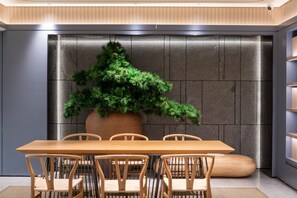 A modern dining area with a long wooden table and six chairs, a large potted plant, and a textured wall. - Ji Hotel (Xi'an)