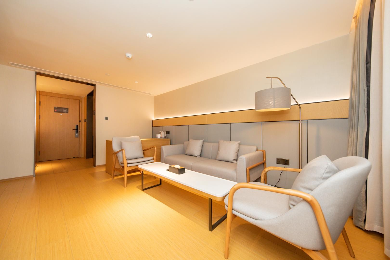 A modern hotel room with a sofa set, two armchairs, a coffee table, and a lamp.