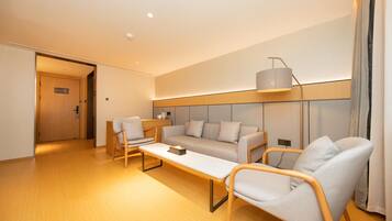 A modern hotel room with a sofa set, two armchairs, a coffee table, and a lamp.