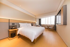 A modern hotel room with a large bed, bedside table, and a small seating area with a table and chairs.