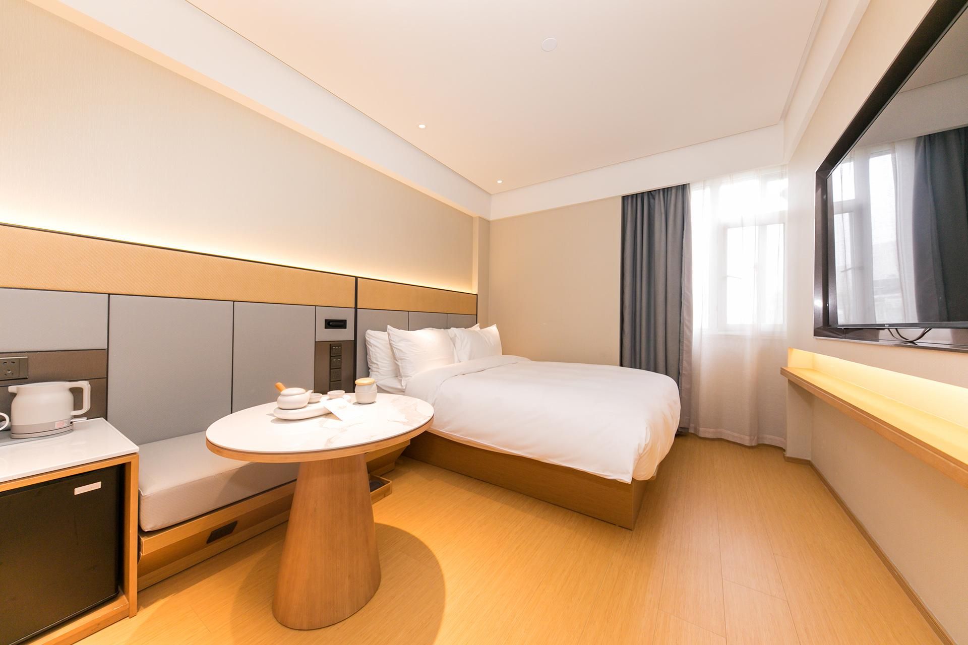 Habitación de hotel con cama, mesita de noche, un pequeño escritorio con silla, espejo y ventana con cortinas.