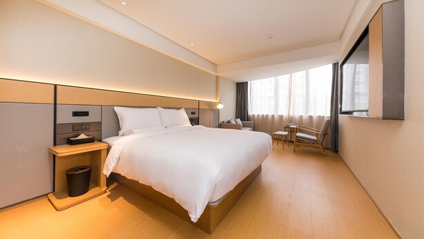 A modern hotel room with a large bed, bedside table, and a small seating area with a table and chairs. - Ji Hotel (Shanghai)