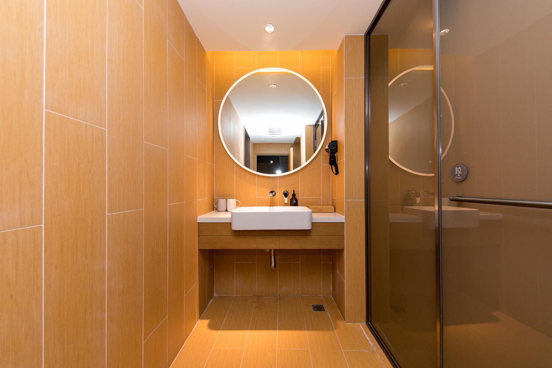 Un baño moderno con cabina de ducha de vidrio, un espejo redondo y un lavamanos blanco.