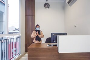 Een persoon staat in een kamer met een houten bureau, een computer en een klok aan de muur.