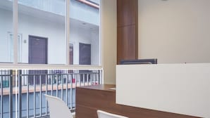 Ein Empfangsbereich mit einem Holzbüro, weißen Stühlen und einem großen Fenster mit Blick auf ein Gebäude mit Hausnummern.