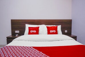Habitación de hotel con cabecera de madera, ropa de cama blanca y almohadas rojas con la palabra 'OYO' escrita en ellas.