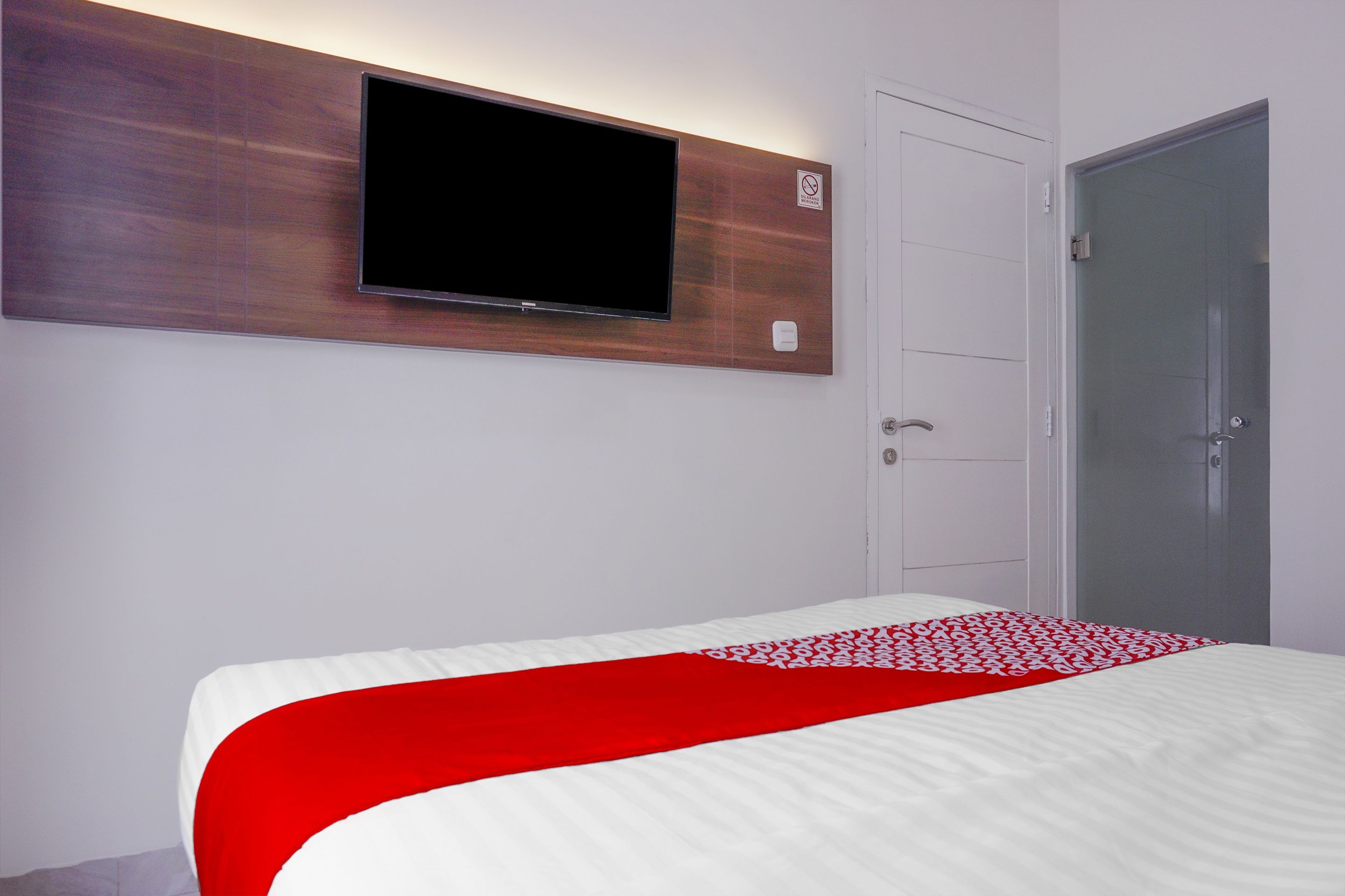 A hotel room with a bed, a mounted TV, a wardrobe, and a door.
